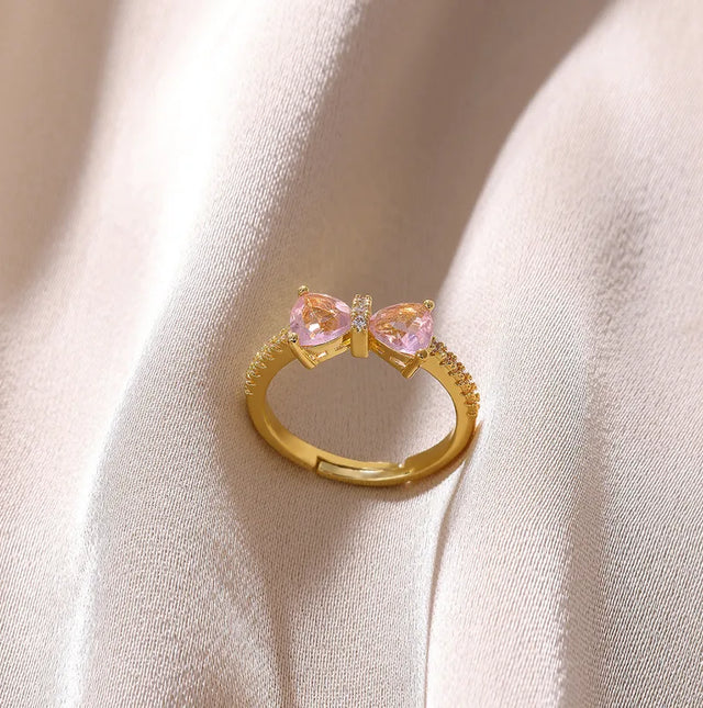 Two gold rings with heart-shaped gemstones on a textured surface