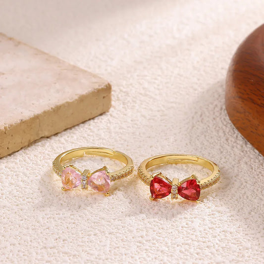 Two gold rings with heart-shaped gemstones on a textured surface