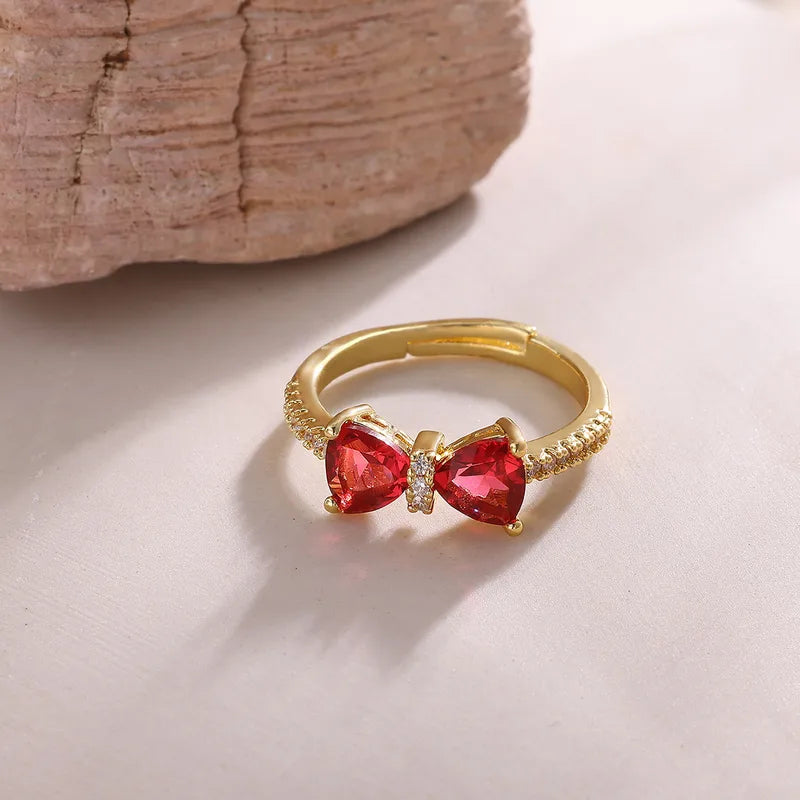 Gold ring with a red gemstone bow design on a light surface.