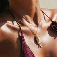 Close-up of a person wearing a gold fish pendant necklace with a blurred background