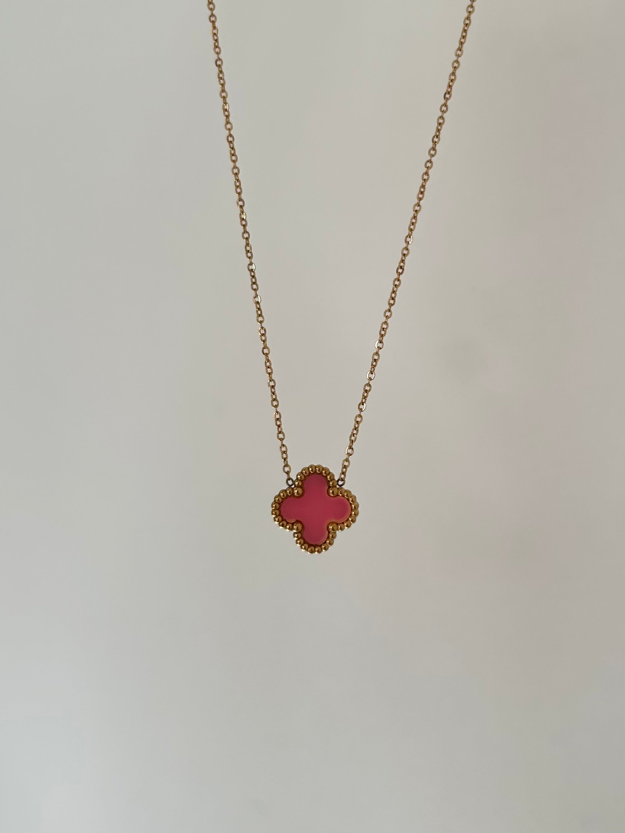 A pink enamel four-leaf clover pendant necklace with a gold-plated chain on a white background.