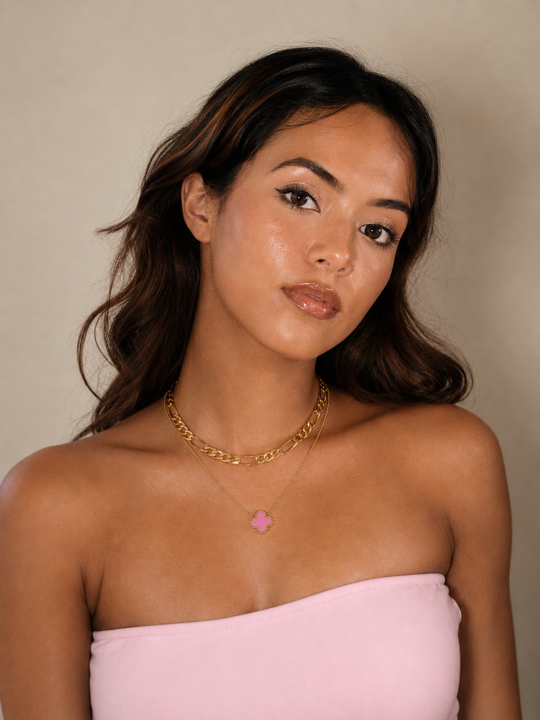 Woman wearing a gold necklace with a heart pendant against a beige background